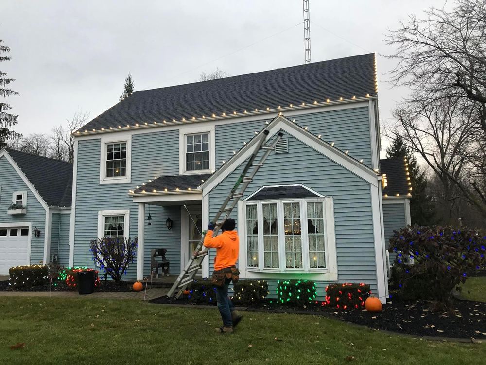 Indiana Christmas Light Installers crew member carrying a ladder to install roofline lights on a home