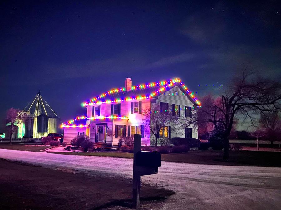 Multicolor Christmas lights on the roofline of a two-story Indiana farmhouse at night